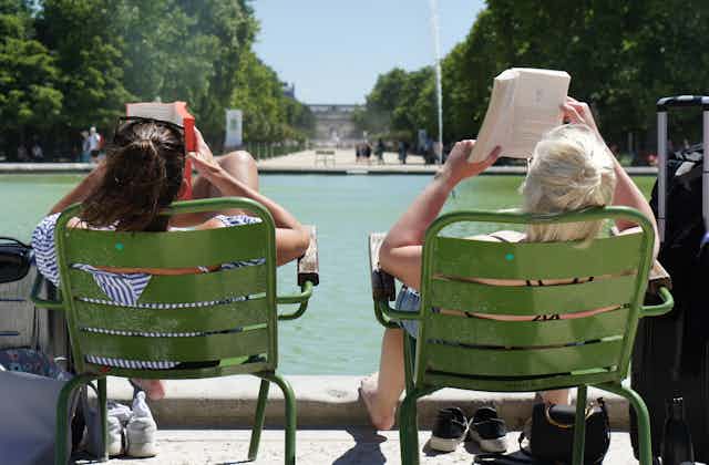The backs of two women in lawnchairs reading by a pool.