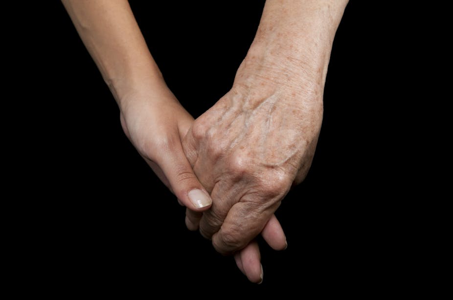 A young person's hand and an old person's hand clasped against a black background.