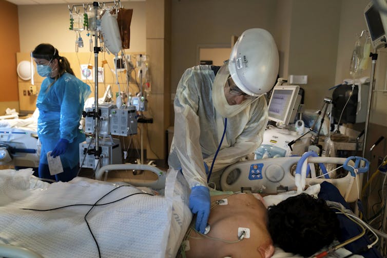 A medical worker in full protective equipment cares for a COVID-19 patient lying face down in a hospital bed.