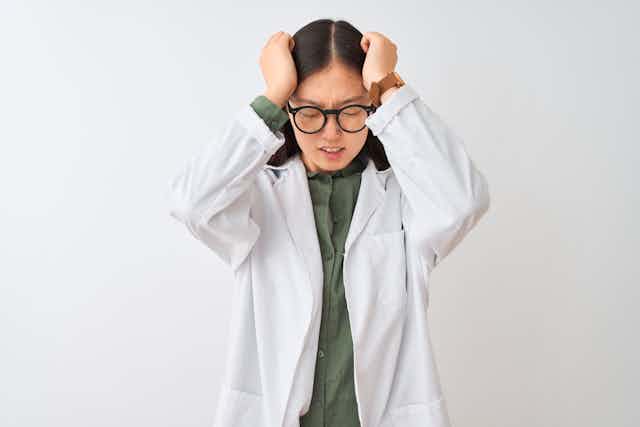 Woman in lab coat holding her head in frustration