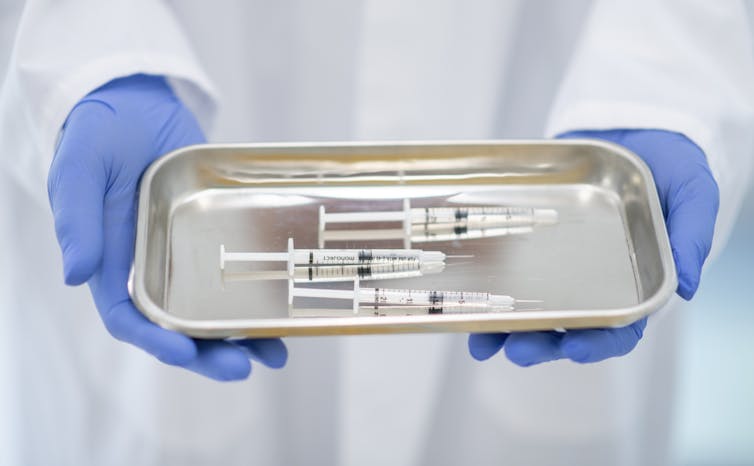 gloved hands holding tray of syringes