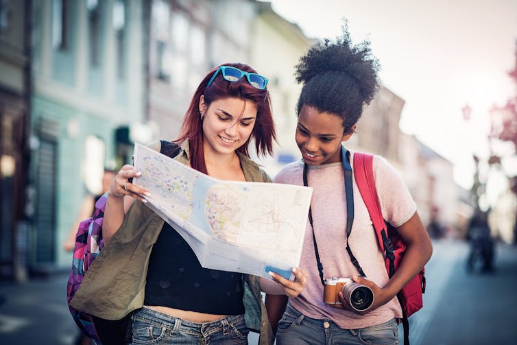 Two teenagers look at a map together while walking in a street