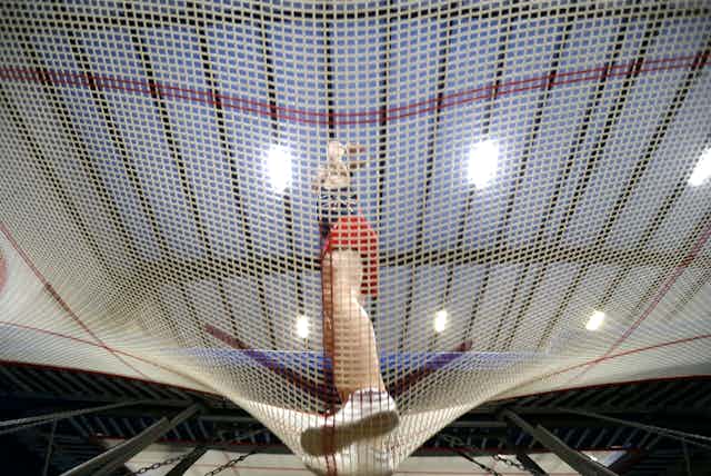 A male gymnast is seen through the holes of a trampoline as he bounces on it. 