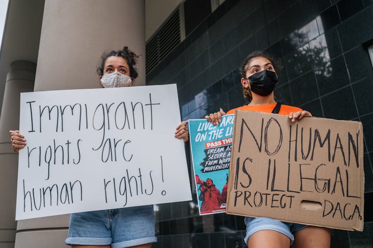Two young women wearing face masks holding signs protesting outside a courthouse