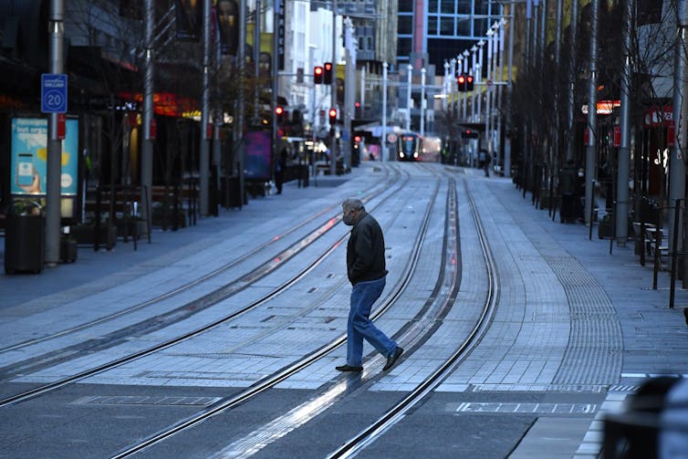 Masked person walking across tram tracks in locked down Sydney