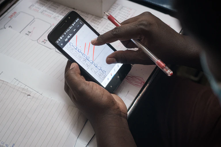 Hands holding a smartphone and a pen, above a school exercise book