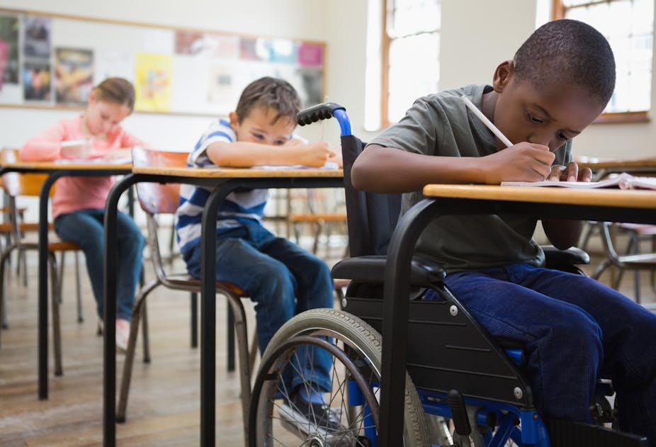 Pupils, one of them in a wheelchair, writing at their desks in a classroom.