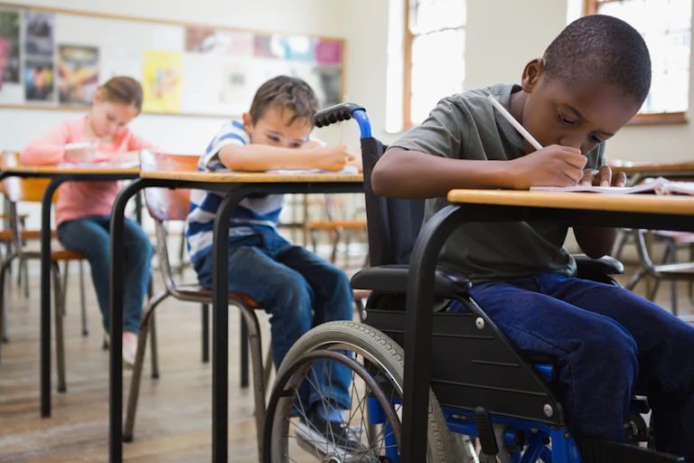 Pupils, one of them in a wheelchair, writing at their desks in a classroom.