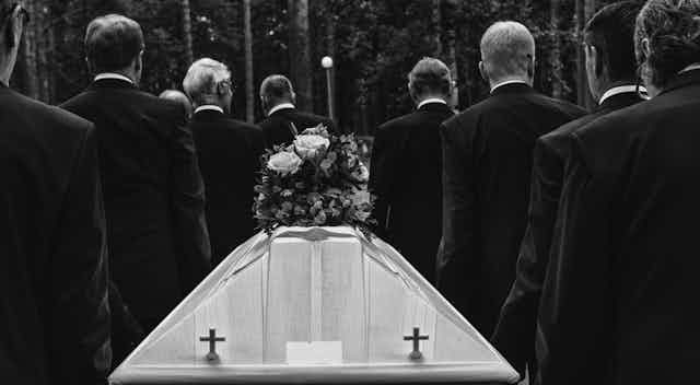 A black and white image of a funeral with eight men carrying the coffin.