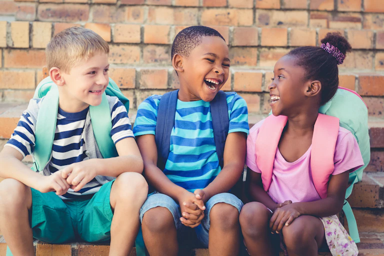 Three children with backpacks sitting on outdoor staircase and laughing
