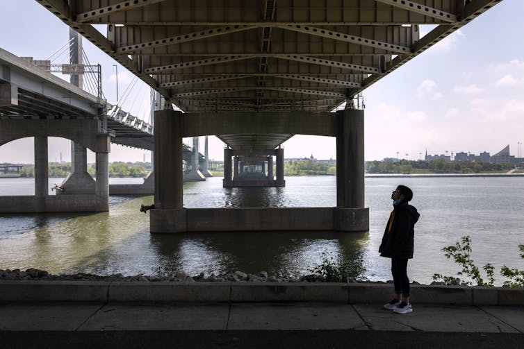 Girl stands under a bridge over a river