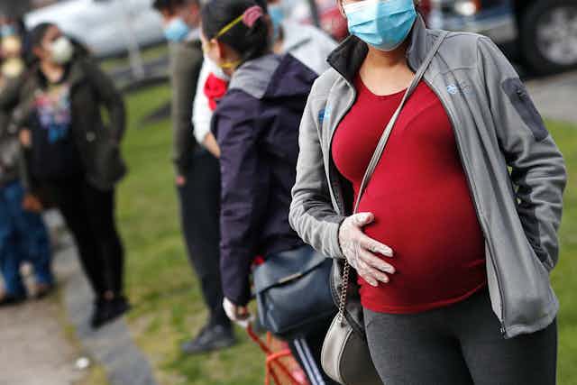 Une femme enceinte fait la file avec un masque.