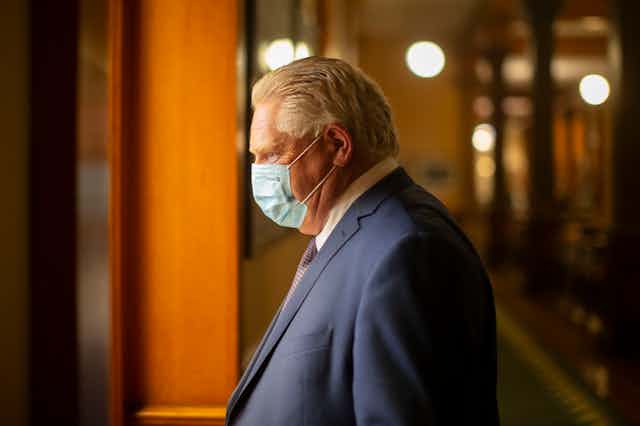 Doug Ford, wearing a mask, walks to his office.