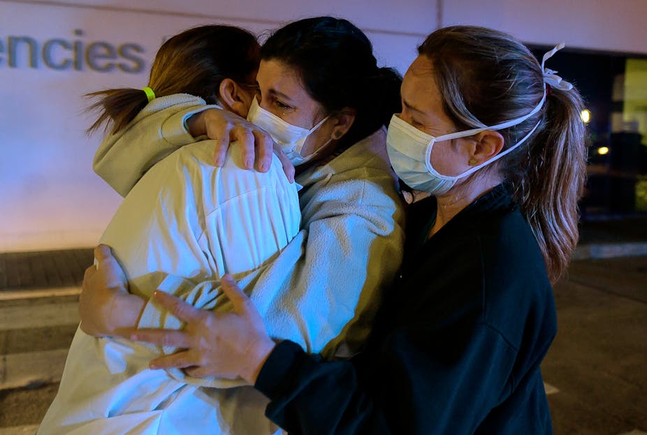 Three healthcare workers in Spain hug each other.