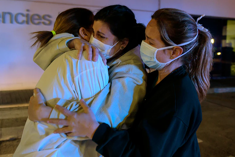 Three healthcare workers in Spain hug each other.