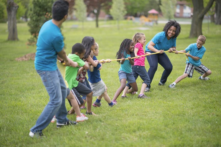 A multi-ethnic group of elementary age children are playing tug-of-war with a rope at the park.