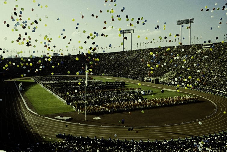 balloons fly over Olympians and spectators during the opening ceremony of the 1964 Summer Olympics at the National Stadium in Tokyo.