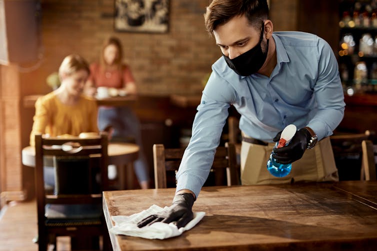 A waiter wipes down a table in a cafe.