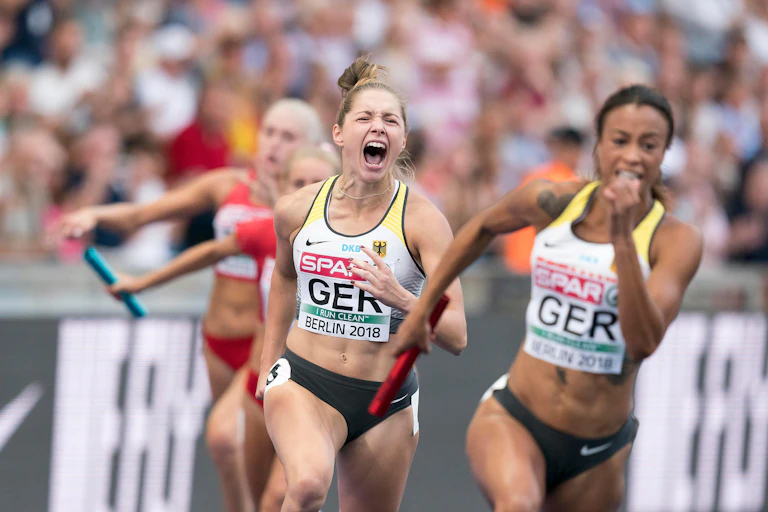 Two female runners compete in a relay track and field race