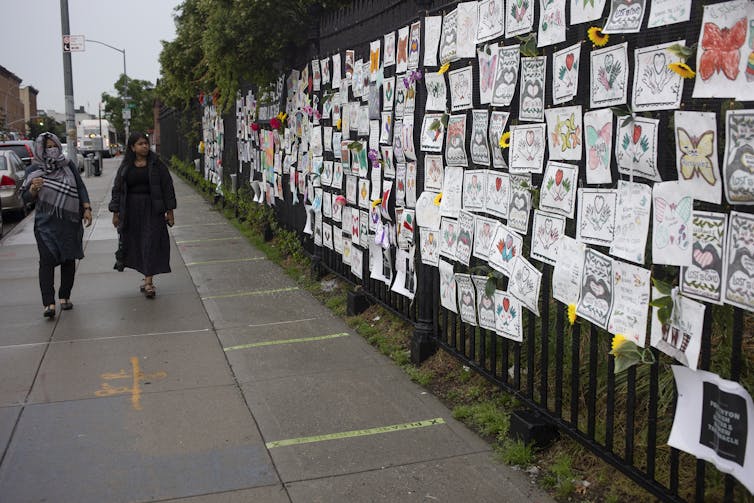 A fence alongside Greenwood Cemetery in Brooklyn, New York, covered with memorial art for those who died of COVID-19.