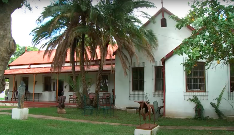 A house with palm tree, old red zinc roof and old facade, church-like on green lawns