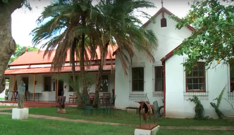 A house with palm tree, old red zinc roof and old facade, church-like on green lawns