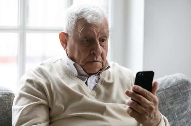 Un señor mayor con cara de susto ante un teléfono móvil.