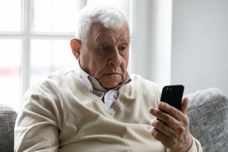 Un señor mayor con cara de susto ante un teléfono móvil.
