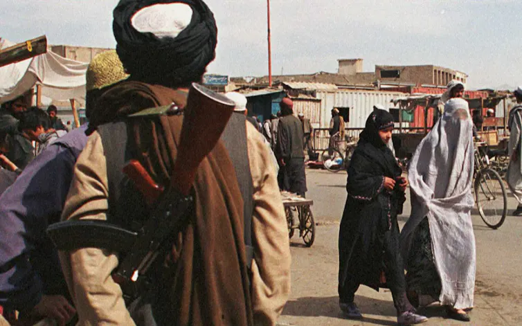Deux femmes afghanes portant des burqas de styles différents passent devant un soldat de la milice fondamentaliste talibane armée