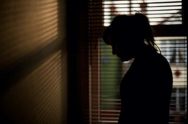 Silhouette of person standing in front of a window.