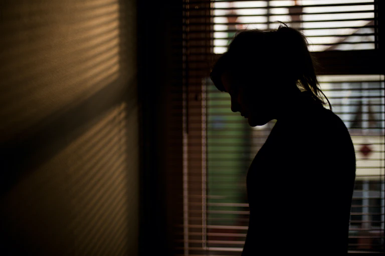 Silhouette of person standing in front of a window.