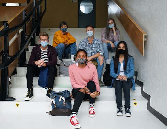 Young people in masks sitting on steps at school