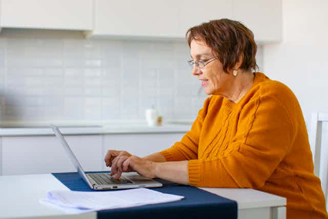 Woman typing on laptop with paper forms next to her.