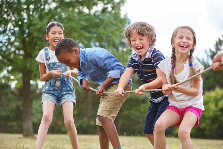 A group of children playing a game of tug-of-war in a park.