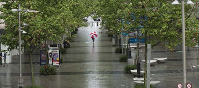 Person walking down a rainy street with red and white umbrella