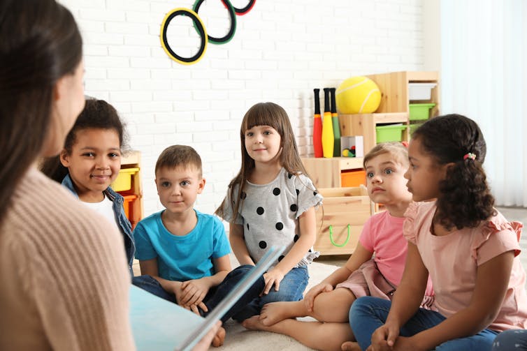 Kindergarten kids listening intently to the teacher as she reads from book.