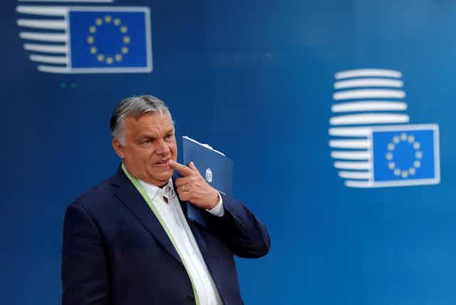 Viktor Orban standing in front of a backdrop printed with EU flags