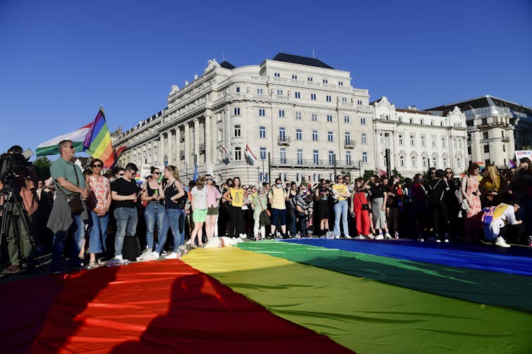 Protestors standing over a giant rainbow flag in front of large building.