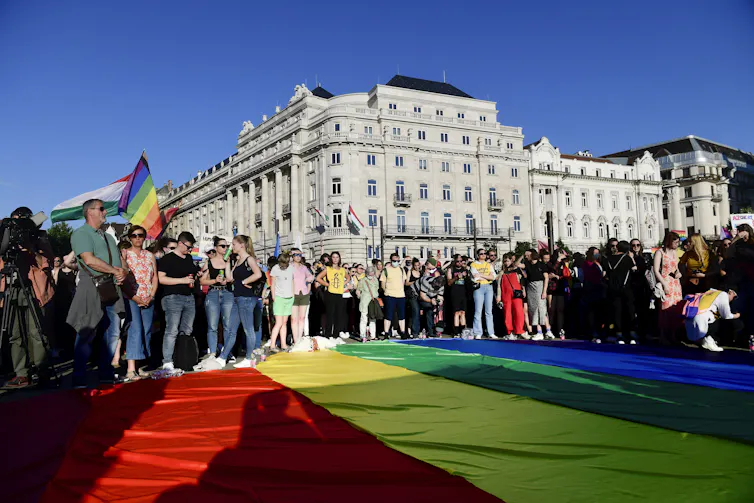 Protestors standing over a giant rainbow flag in front of large building.