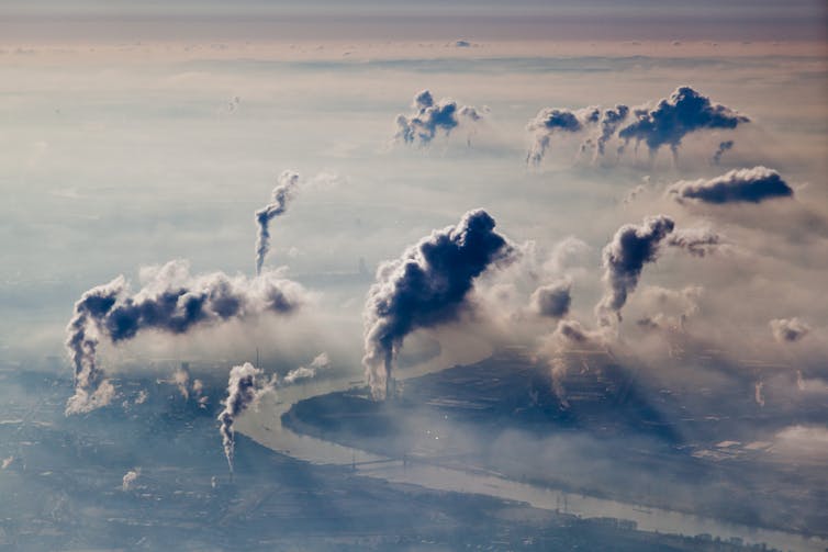 Factory smokestacks emitting clouds of pollution over a hazy skyline.