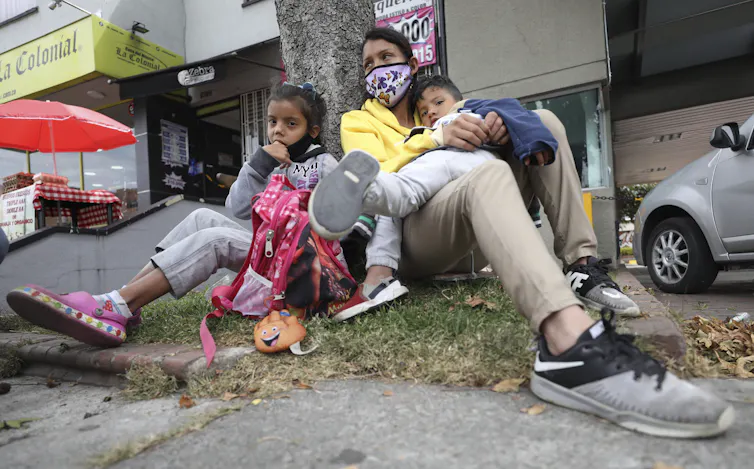 Woman sits with her two children at the base of a tree
