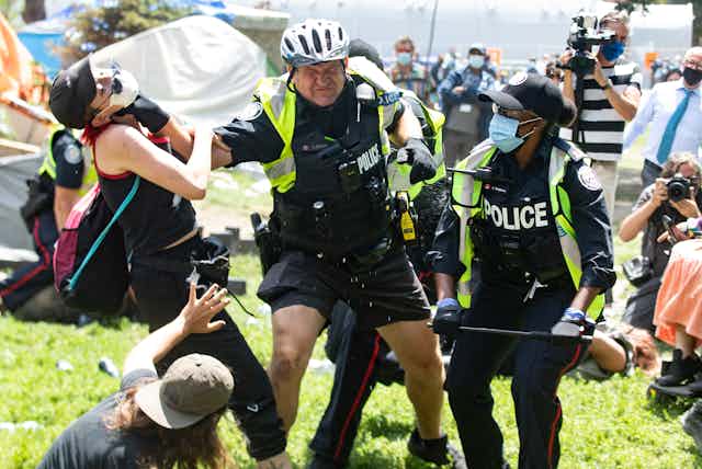 Police grabs encampment supporter by the neck at Lamport Stadium Park