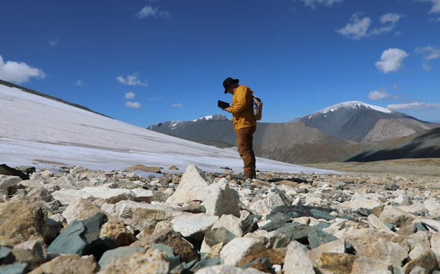 man stands on rocky ground at the melting edge of a glacier