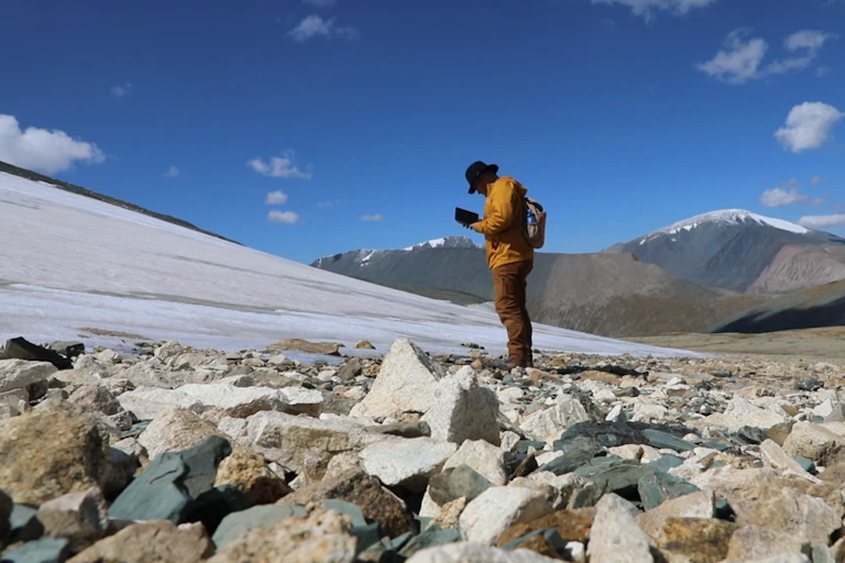 man stands on rocky ground at the melting edge of a glacier