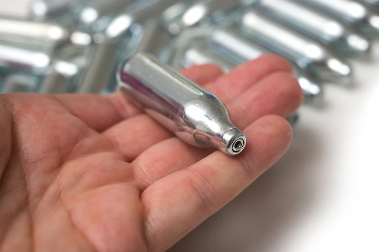 A canister of nitrous oxide sits in a person's hand.