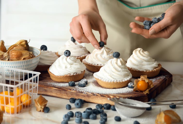 A person preparing tarts with whipped cream on top.