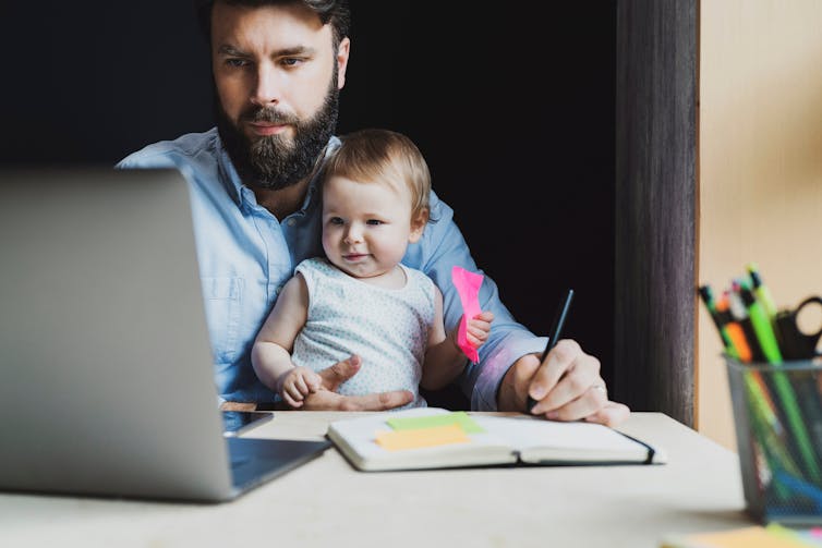 Parents sits with young child on lap in front of laptop as he studies online