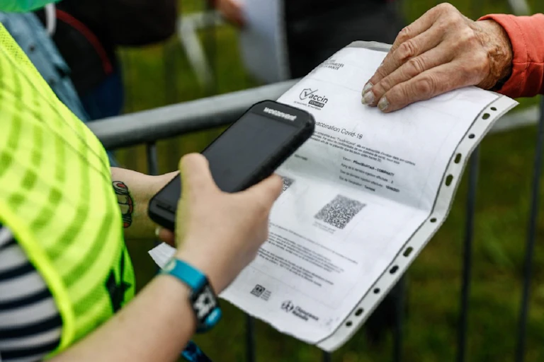A person hands over a print-out of their health pass to an official.