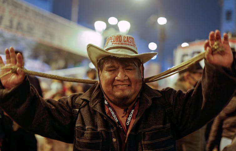 Man in cowboy hat that says 'Pedro Castillo' smiles at the camera on a crowded street