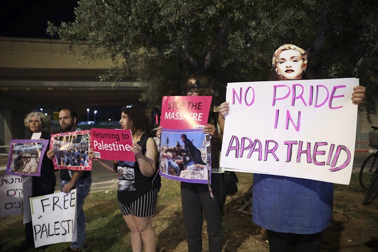 Um manifestante em primeiro plano segura uma placa que diz "nenhum orgulho do apartheid", enquanto outros carregam placas como Palestina livre durante um protesto fora do Festival Eurovisão da Canção 2019 em Tel Aviv, Israel